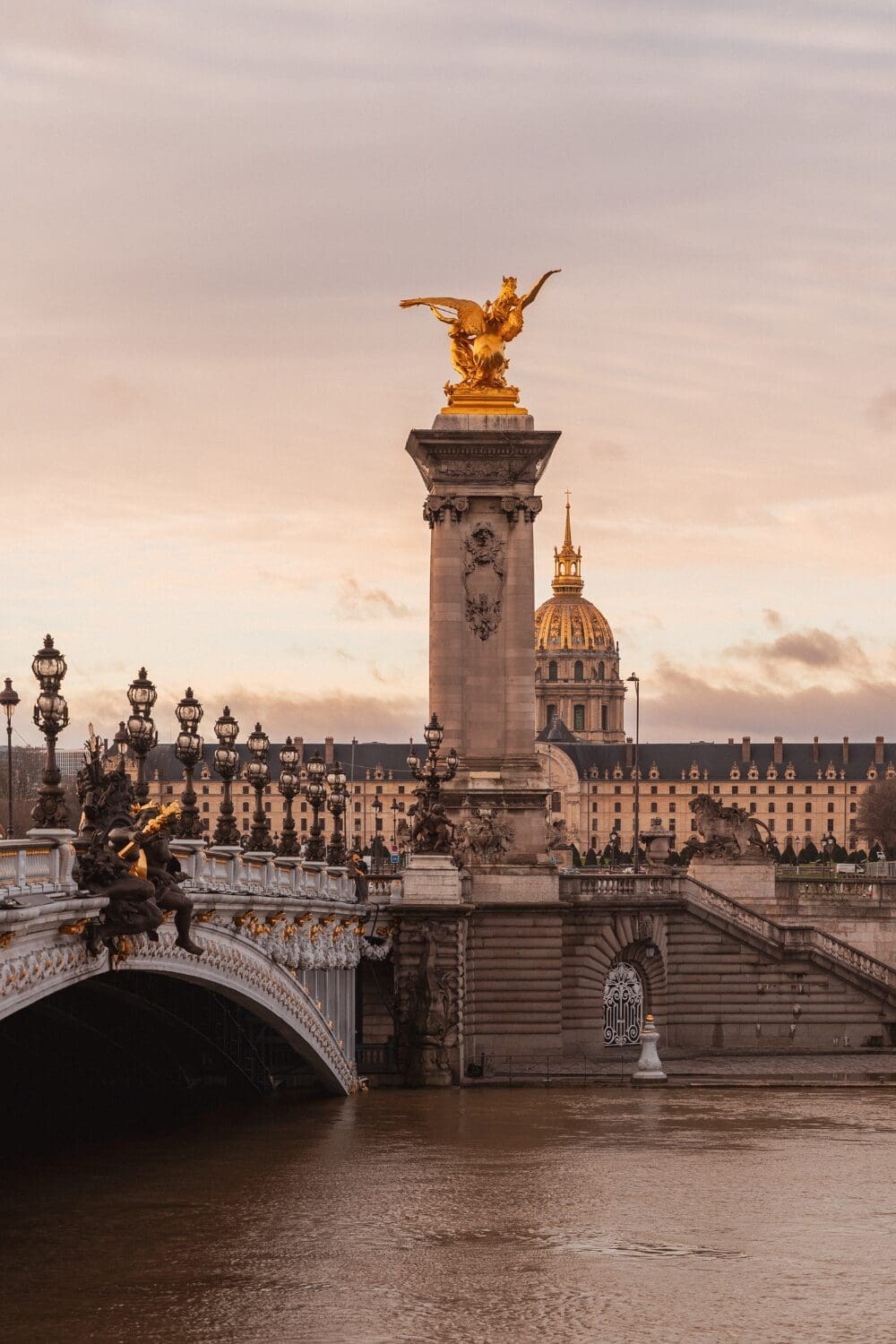 Pont Alexandre III bridge in Paris at golden hour with ornate gold statues and Les Invalides dome glowing in background, Paris France