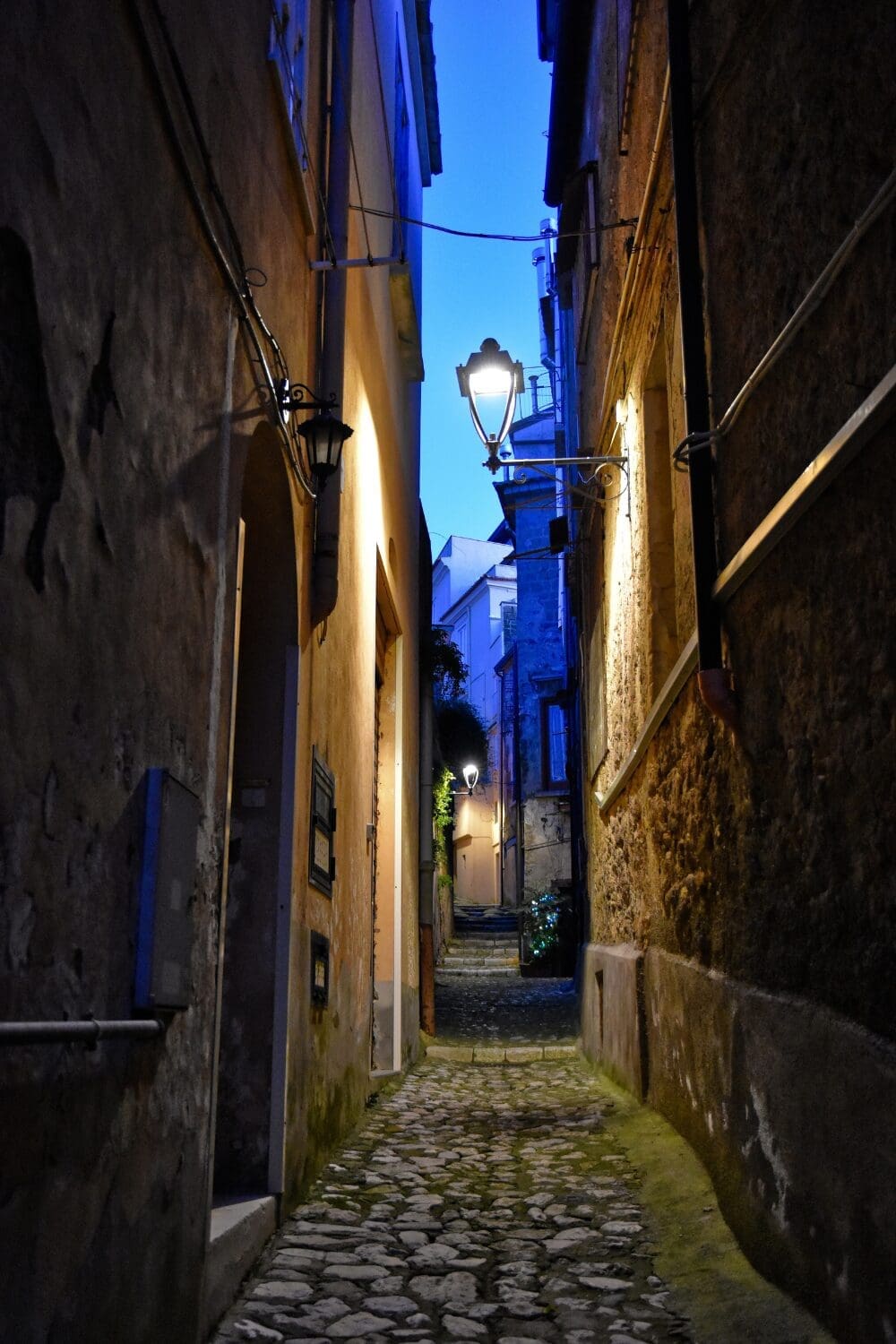 Narrow cobblestone alley at twilight in French village with blue hour lighting and stone steps, literary travel France