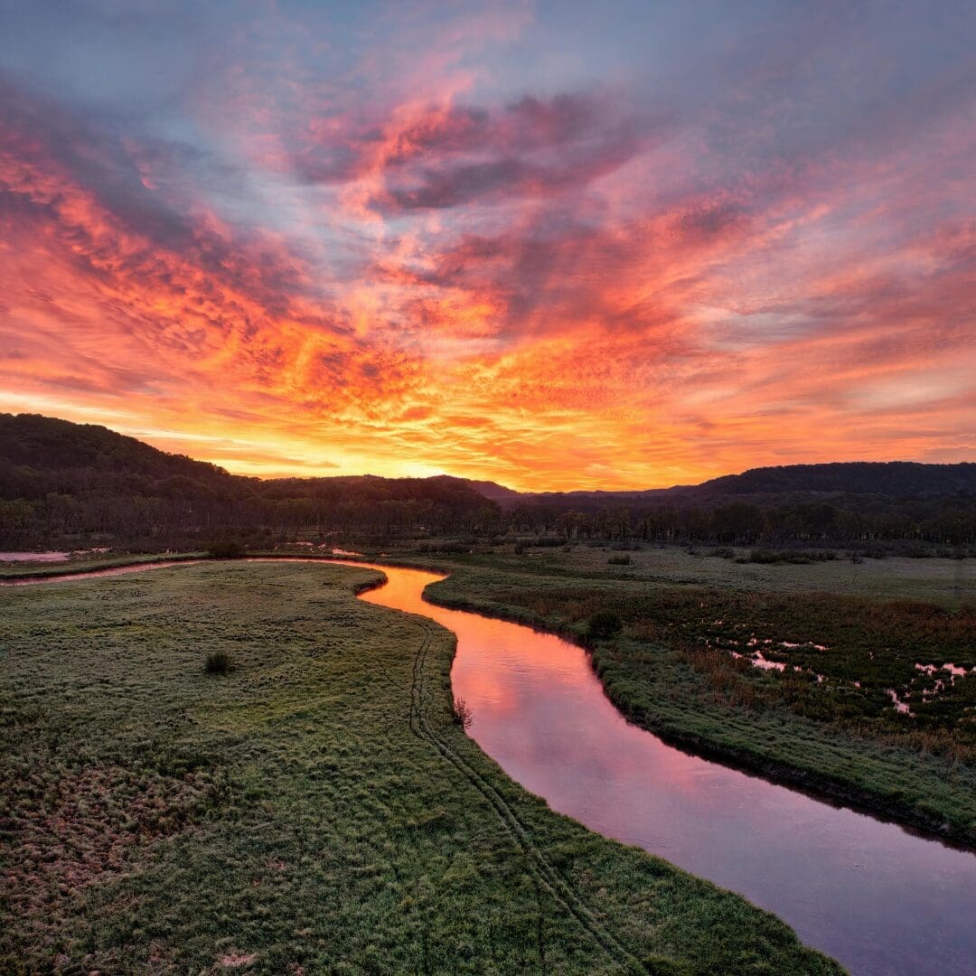 Dramatic winding river through green French countryside at sunset with fiery orange and red sky, Loire Valley France