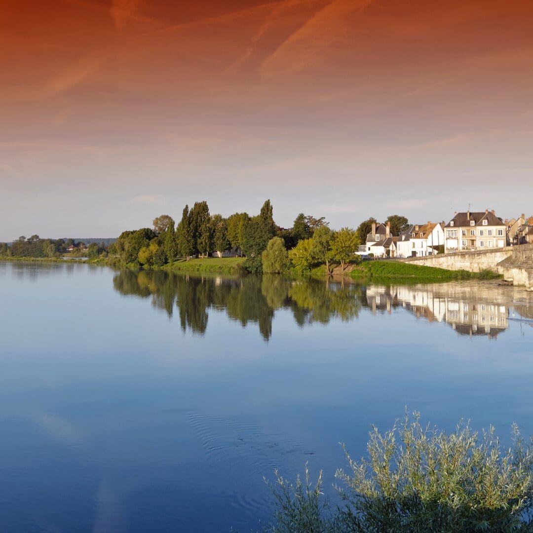 Loire Valley river at sunset with château silhouette and warm peach sky reflecting on calm water, France travel 2027