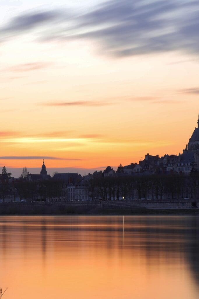 Loire Valley river at sunset with château silhouette and warm peach sky reflecting on calm water, France travel 2027