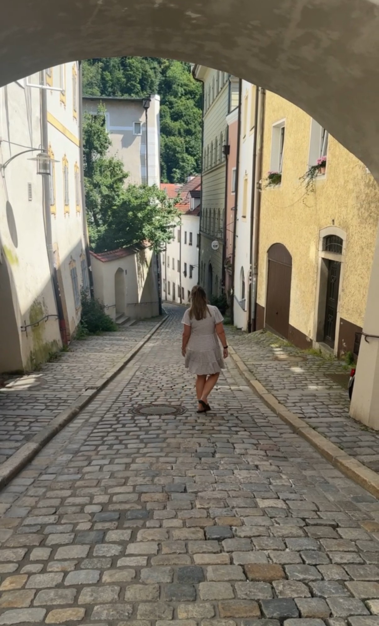 Woman walking through a cobblestone stone arch alleyway in Germany, enneagram travel destinations guide by Winds and Waves Travel