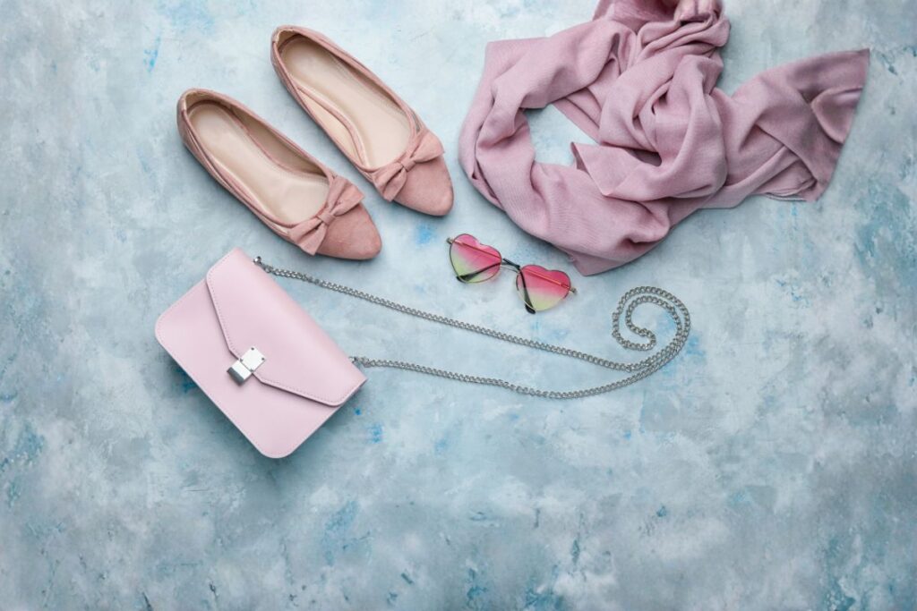 Blush pink flats, scarf, sunglasses, and crossbody bag flat lay of Paris travel accessories