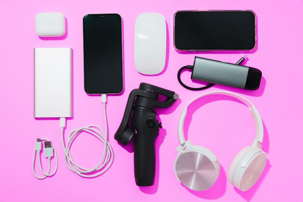Phone, headphones, portable charger, and travel tech essentials flat lay on a pink background